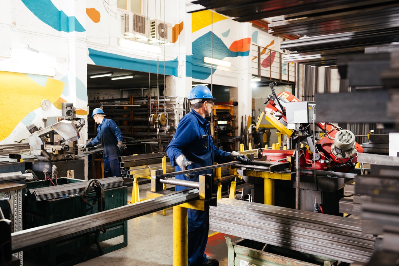 Unrecognizable male workers in protective helmets and uniforms working with machinery on metal factory